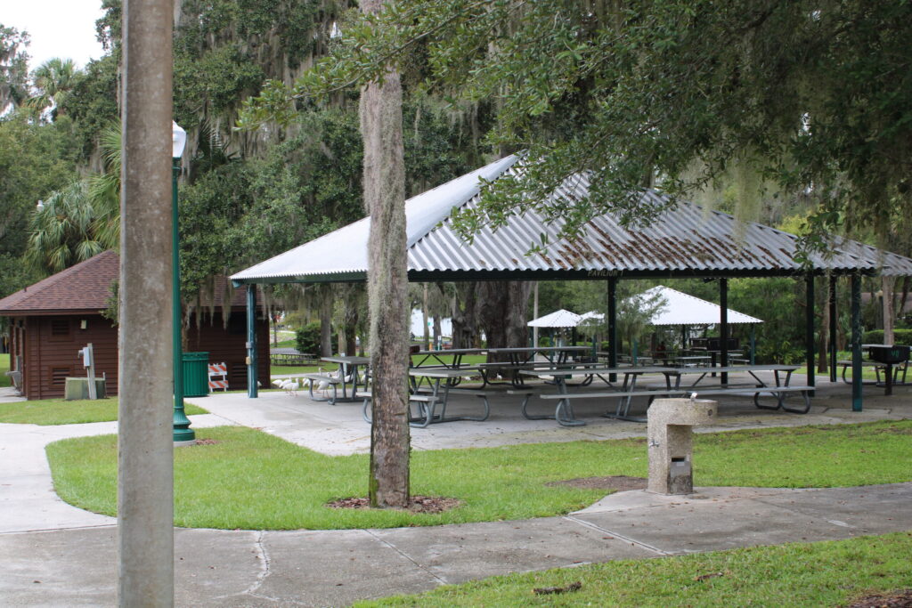 Shaded picnic pavilions and grilling areas in Gilbert Park under large oak trees.